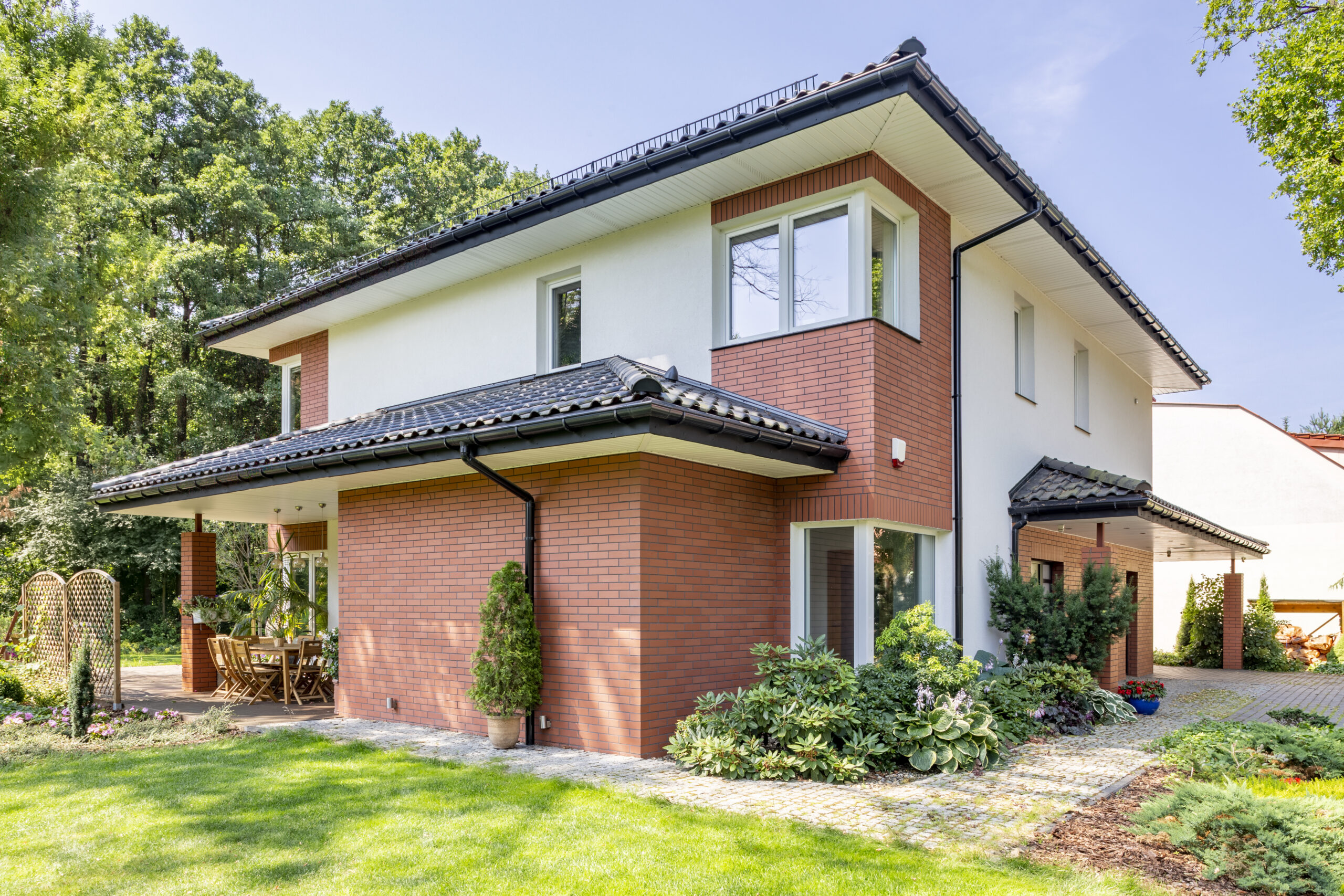 Red brick house with terrace and green grass and trees during summer